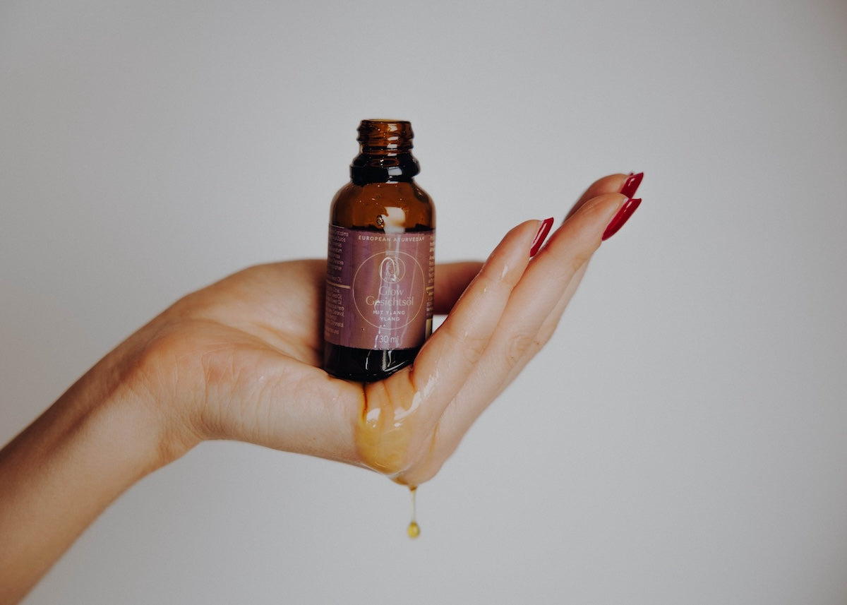 Glow Gesichtsöl mit Pipette neben Blumen – ayurvedisches Gesichtsöl mit natürlichen Inhaltsstoffen für gesunde Hautpflege.