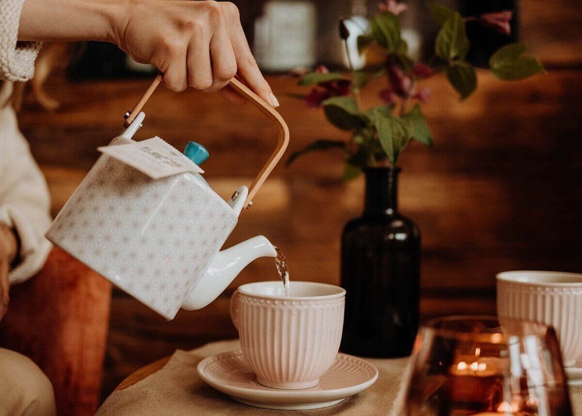 Ayurvedischer Pitta Tee wird aus einer Teekanne in eine Tasse eingeschenkt.