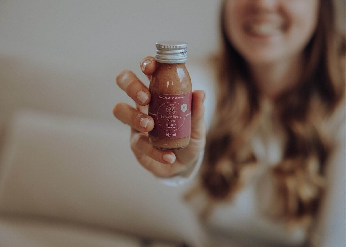 Hand hält Power Berry Shot von European Ayurveda – biologischer Ayurveda Shot mit Ingwer, Himbeere und Zitrone.